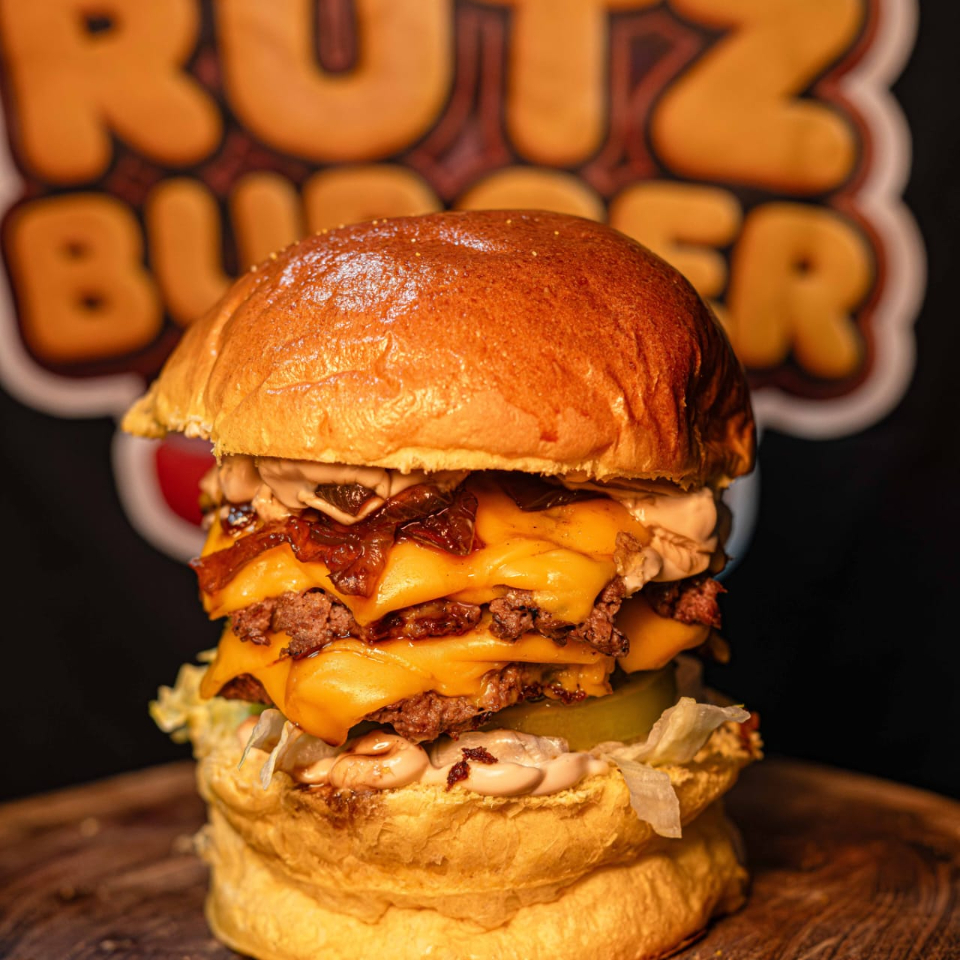 Pão brioche selado, duas carnes tostadinhas de 80g, queijo cheddar, cebola caramelizada, alface, tomate, picles e molho onion black roots.