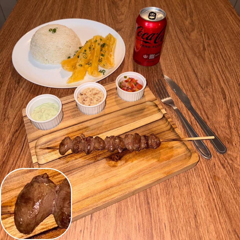 Espeto de coração de frango acompanhado por arroz, mandioca, vinagrete, farofa crocante e molho verde.