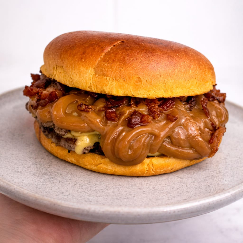 Pão de Brioche, 2 carnes smash de 100 gramas cada , queijo prato , doce de leite moça e bacon.