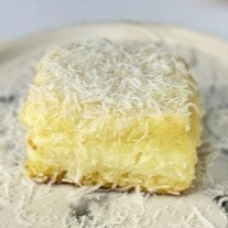 Uma porção de bolo gelado, bem moladinho, com recheio de coco e coberta com flocos de coco.