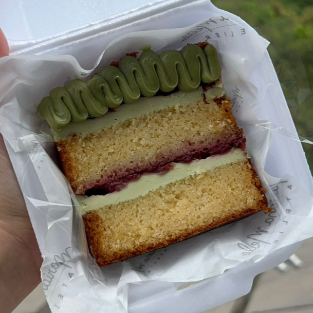 Fatia de bolo de massa amanteigada de baunilha recheada com ganache de pistache e geleia de morango. Decorada com creme de pistache.