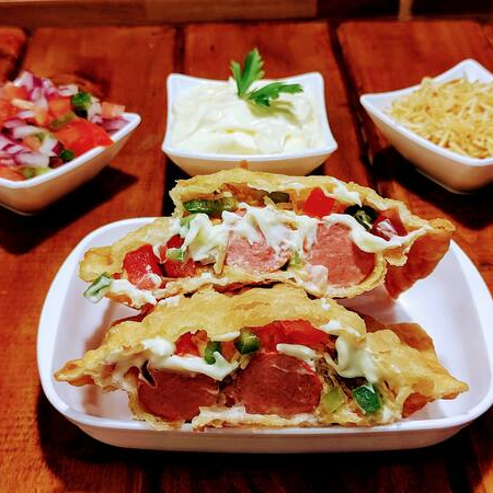 Um delicioso pastel quadrado com duas salsichas, molho cru de tomate, cebola e pimentão verd, com molho de alho especial da casa e batata palha.