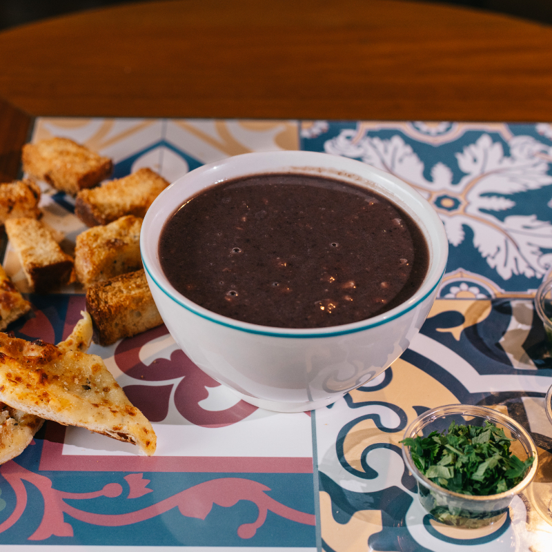 A Sopa de Feijão, da categoria Sopas, é uma verdadeira explosão de sabores, perfeitamente combinados para aquecer e satisfazer. Esta deliciosa receita é preparada com feijão selecionado, cuidadosamente cozido até atingir a consistência perfeita. A calabresa e o bacon, ingredientes de alta qualidade, são adicionados para trazer um toque de defumado e intensificar o sabor. A seleção de condimentos, criteriosamente escolhidos, agrega ainda mais aroma e profundidade ao prato. Uma escolha irresistível para uma refeição reconfortante e cheia de sabor.