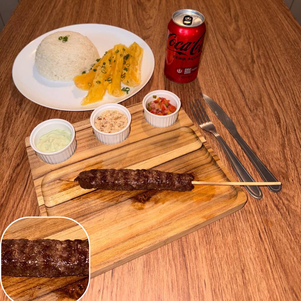 Espeto de kafta (patinho e costela) acompanhado por arroz, mandioca, vinagrete, farofa crocante e molho verde.