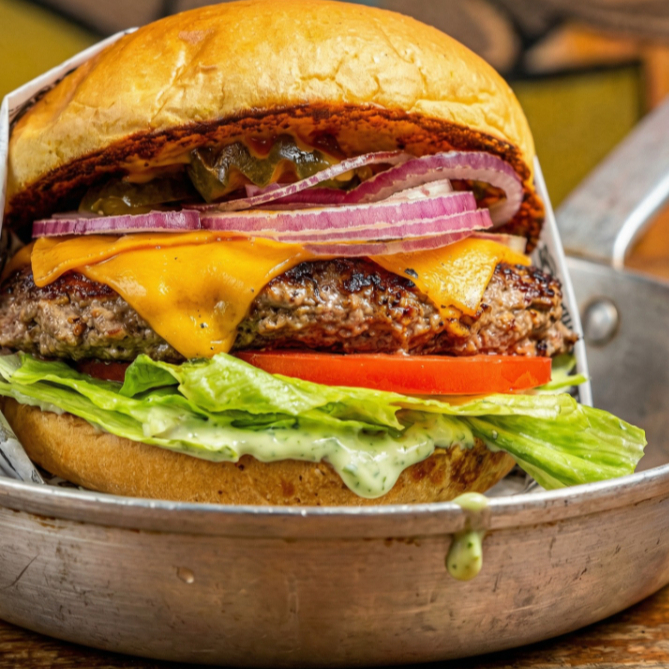 Pão brioche tostado na chapa com manteiga, hamburguer artesanal de aprox 160g, queijo cheddar fatiado, alface, tomate, picles, cebola roxa e maionese da casa.