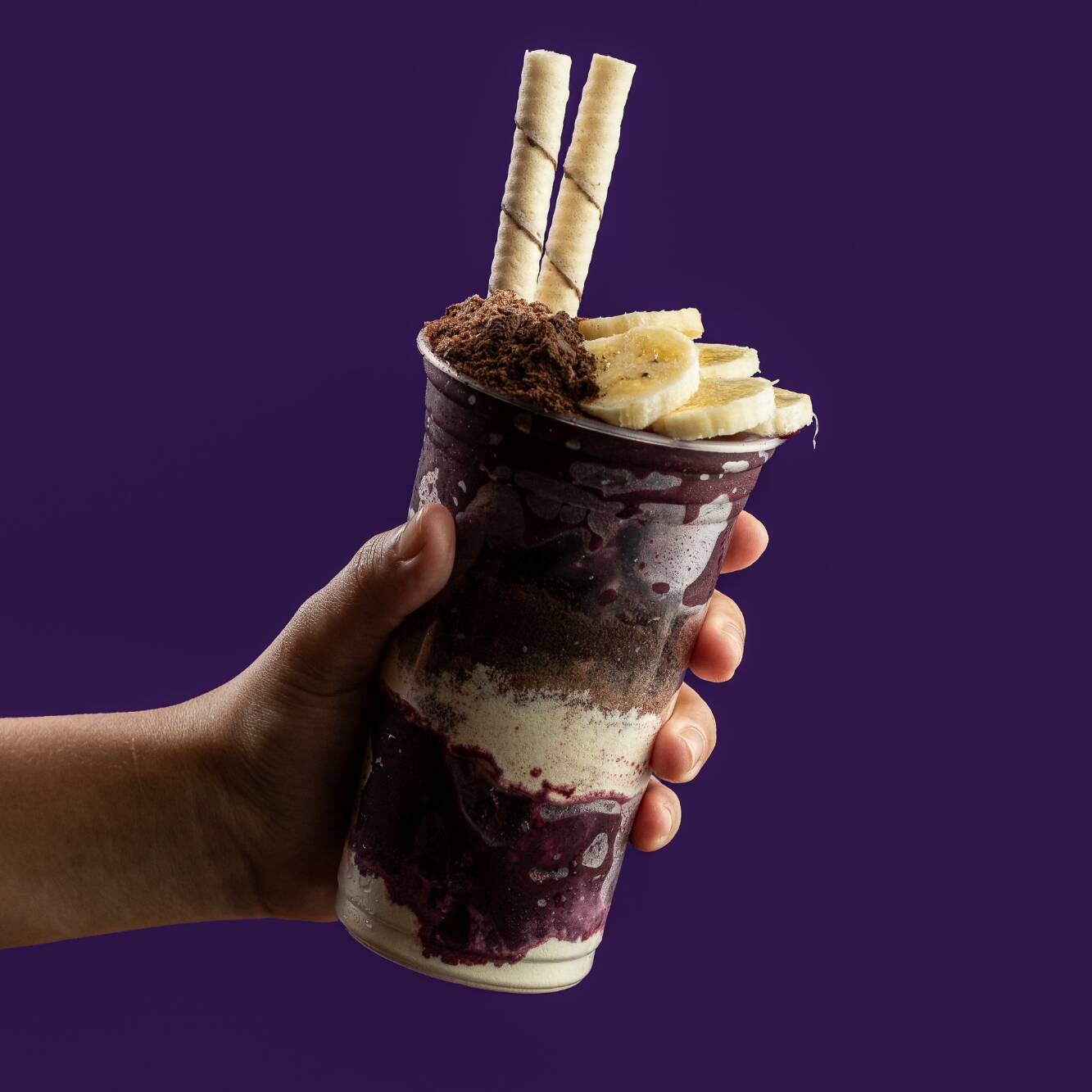 Creme de açaí acompanhado de banana, leite condensado, leite em pó, Oreo granulado e Ovomaltine no pote, e mais tubetes.