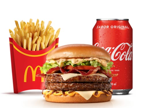 Dois hambúrgueres de carne 100% bovina, méquinese, a exclusiva maionese especial com sabor de carne defumada, alface e tomate, fatias de bacon, queijo processado sabor emental, molho especial e cebola ao molho shoyu, tudo isso no pão tipo brioche trazendo