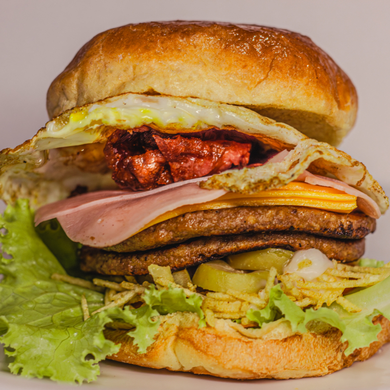 Se você está em busca de uma refeição deliciosa e cheia de sabor, o X Tudo Turbo é a escolha perfeita! Com uma combinação incrível de ingredientes frescos, este lanche é a verdadeira explosão de sabores que vai satisfazer sua fome em qualquer hora do Dia.
Imagine isso: um pão macio recheado com dois hambúrgueres suculentos, um ovo frito perfeito, presunto, bacon crocante e queijo derretido. Para dar aquele toque especial, adicionamos alface e tomate frescos, Catupiry cremoso e azeitonas. E para completar, uma generosa porção de batata palha que traz a crocância ideal!