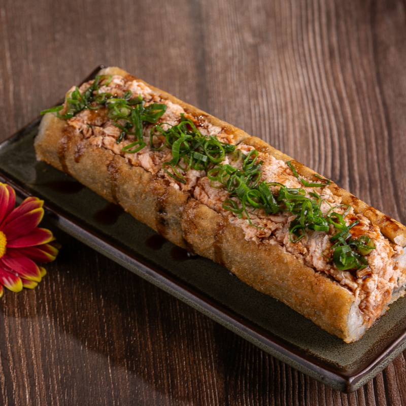 Hot empanado cortado ao meio com recheio de cream cheese, salmão em cubos e finalizado com molho de pimenta, cebolinha e gergelim.