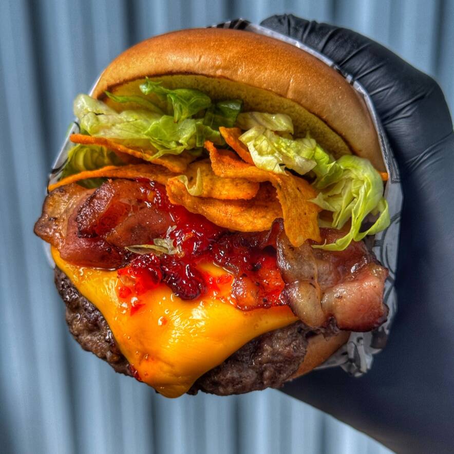 O Netuno é uma experiência de sabores intensos e texturas surpreendentes, começando pelo nosso pão brioche premium, que é extremamente amanteigado, macio e selado na medida certa para garantir uma estrutura impecável. O hambúrguer artesanal de 150g vem acompanhado de uma fatia generosa de queijo cheddar derretido e bacon crocante, mas o grande diferencial está na combinação da nossa geleia de pimenta artesanal com a crocância dos nachos. Para equilibrar toda essa intensidade, o lanche é finalizado com alface americana fresca, entregando um contraste perfeito entre o adocicado, o picante e o frescor em cada mordida.