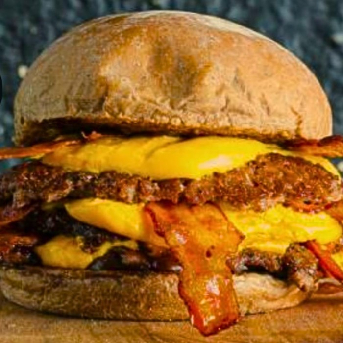 Pão australiano, dois burger de carne bovina de 90g, queijo cheddar cremoso, fatias de bacon e molho barbecue. Imagem meramente ilustrativa.