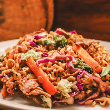 Macarrão estilo "yakisoba" flambado no molho à base de shoyu, azeite e trio de cogumelos com folhas e legumes. Obs: Este alimento é preparado em recipiente separado de todas as nossas outras receitas e segue todas as atribuições necessárias de respeito as regras de preparo de alimentos da Comunidade Vegana)