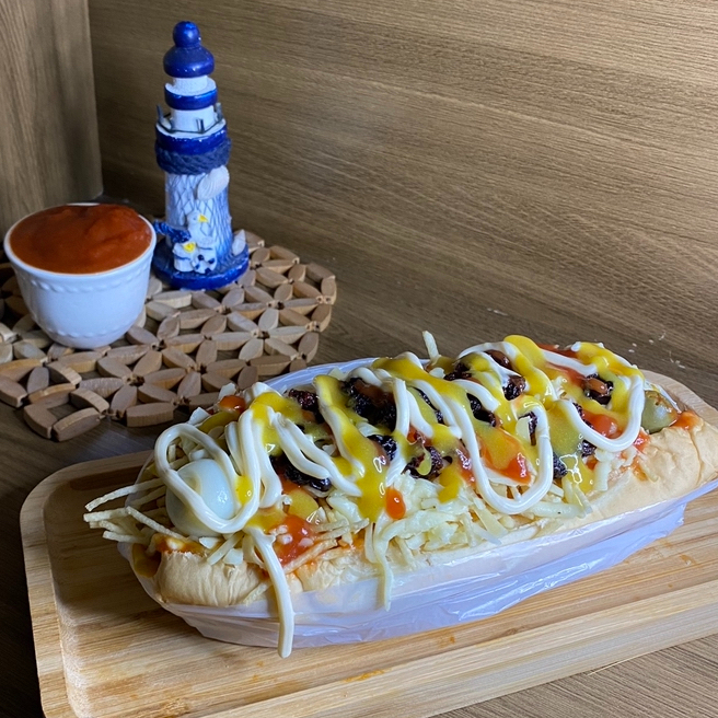 Acompanha: Pão, salsicha, Molho, Milho, Ervilha, Maionese, Mostarda, Ketchup, Batata Palha, Queijo Mussarela, Passas e Ovo de Codorna.