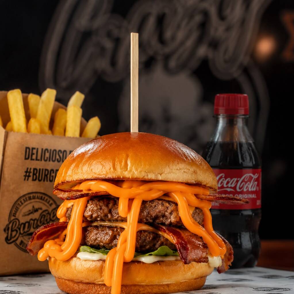 . Pão brioche, 2x hambúrgueres de 150g cada, queijo cheddar e cheddar cremoso, 4fatias de bacon crocante, alface, cebola roxa, picles e maionese caseira. Acompanha batata frita e Coquinha 200ml