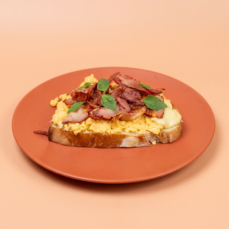 Pão italiano de fermentação natural com ovos cremosos, uma camada de requeijão, muito bacon e folhas de manjericão.
