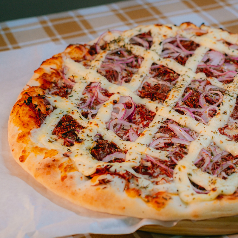 Para os amantes da culinária regional: uma pizza generosa que une a intensidade do charque desfiado à suavidade do requeijão. Acompanhada de cebolas fatiadas e orégano, criando um contraste de sabores que é pura tradição.