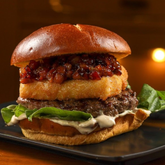 Pão brioche caramelo macio, hambúrguer suculento de 160g no ponto perfeito, geleia de bacon caramelizada com cebola em cubos trazendo um mix de sabores, folhas de rúcula fresca pra equilibrar e uma lapa absurda de queijo mussarela empanada, crocante por fora e derretendo por dentro.