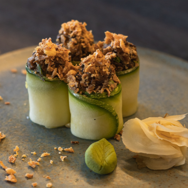 Abobrinha branqueada envolvendo arroz e tartar cremoso de shimeji, finalizado com cebola crispy.