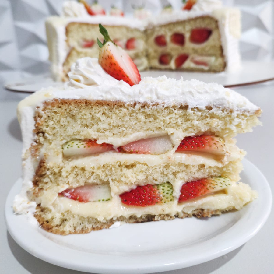 Fatia de Torta Ninho com Morango: massa fofinha de baunilha, creme de Ninho bem cremoso e morangos frescos em camadas. Uma fatia geladinha, leve e irresistível, com o equilíbrio perfeito entre doce e fruta.