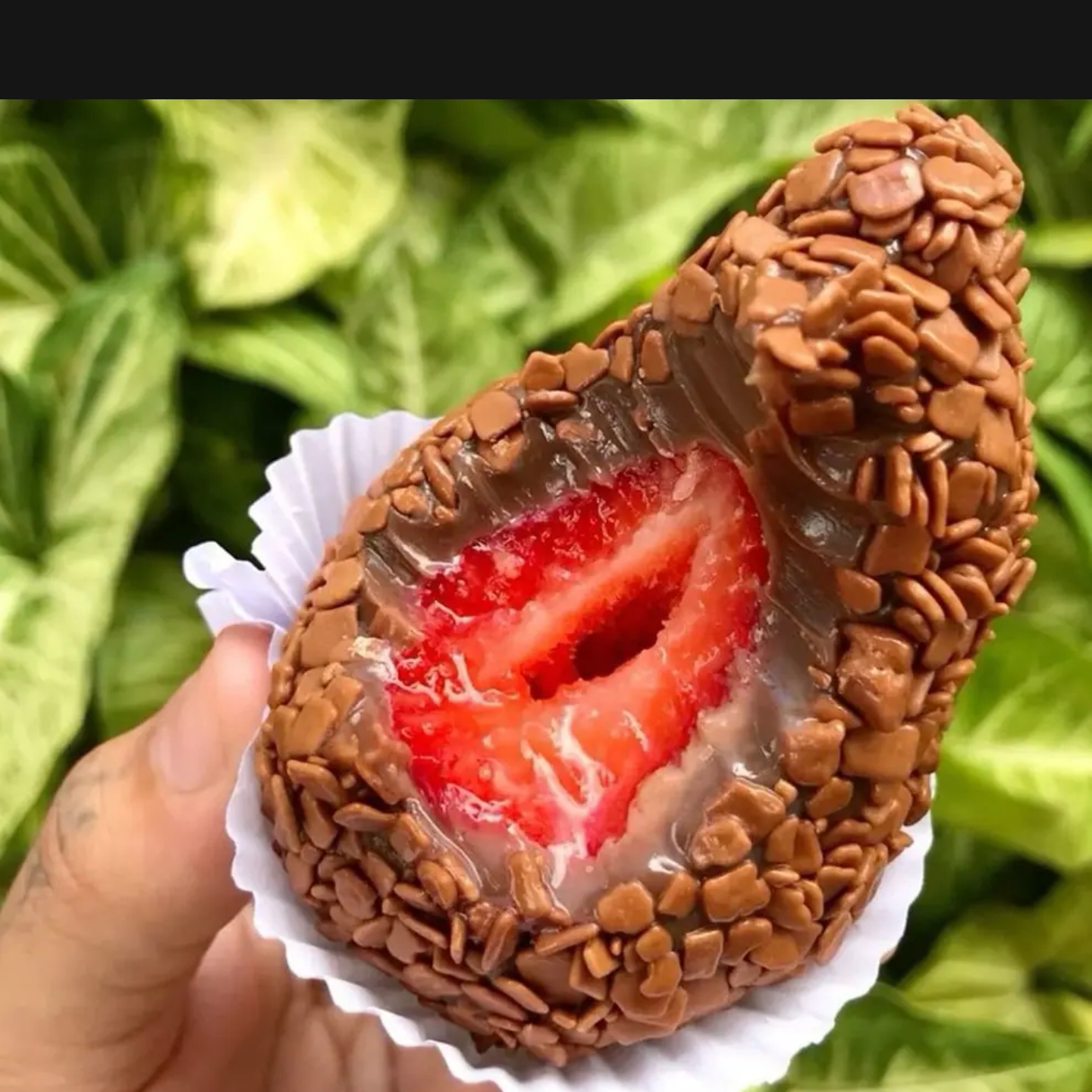 Um delicioso coxinha de morango coberta com chocolate e granulado,