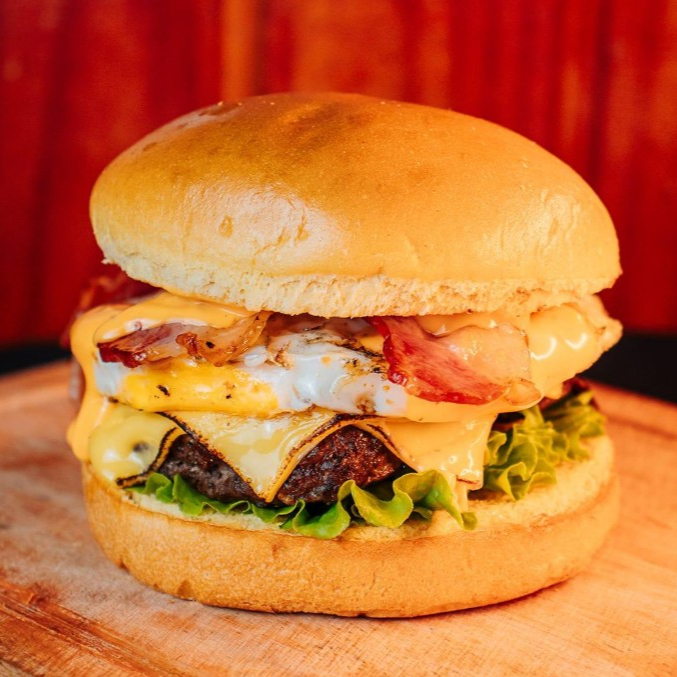 Burguer Artesanal 150g com queijo prato derretido a perfeição, ovo, bacon crocante, alface, tomate e maionese da casa no pão de brioche. Uma combinação suculenta e cheia de sabor!