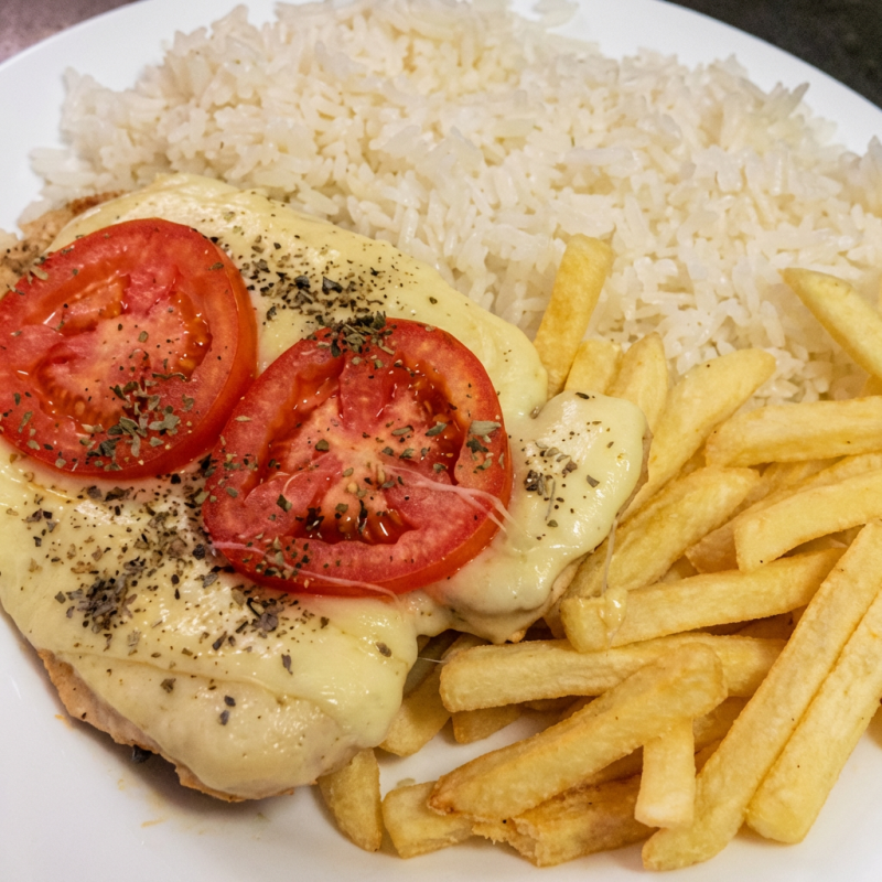 Acompanha: Arroz, feijão, macarrão alho e oleo, frango empanado coberto com queijo, molho de tomate, tomate e orégano