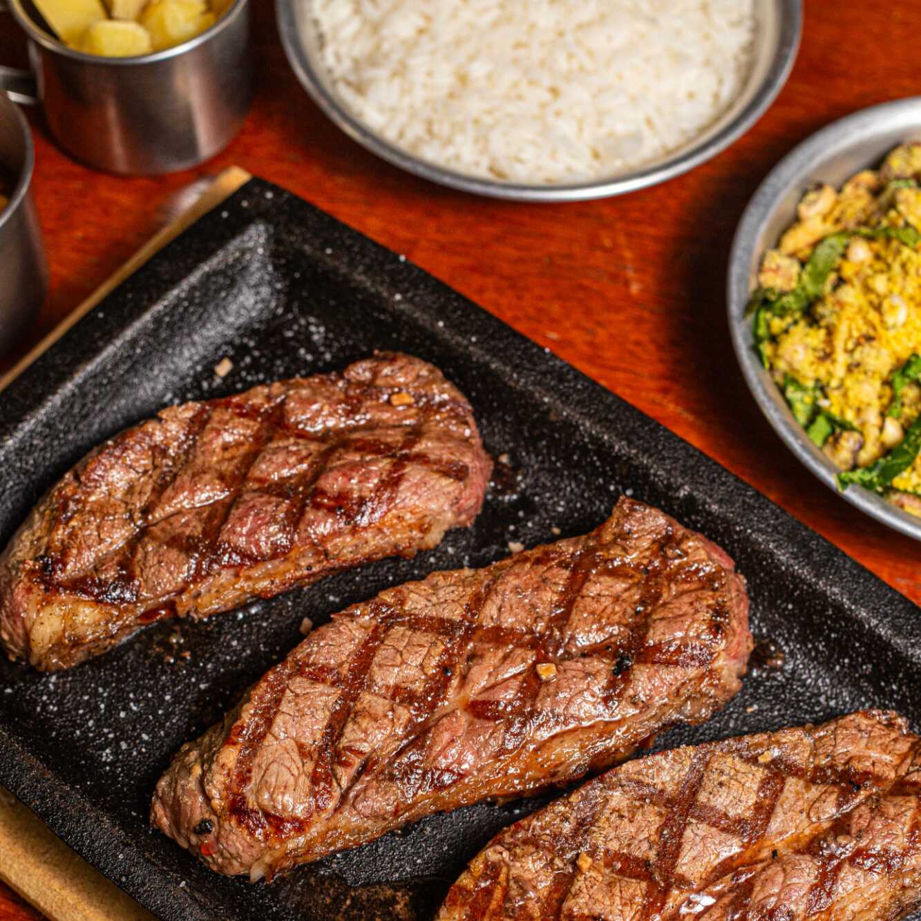 Picanha maturada grelhada na brasa, preparada no ponto ideal para manter a suculência e finalizada com sal de parrilla, realçando o sabor intenso da carne.
Acompanha arroz, feijão tropeiro, farofa crocante, vinagrete fresco e macaxeira cozida na manteiga.
Combina perfeitamente com uma Heineken Long Neck bem gelada ou uma Coca-Cola Zero 1l.
