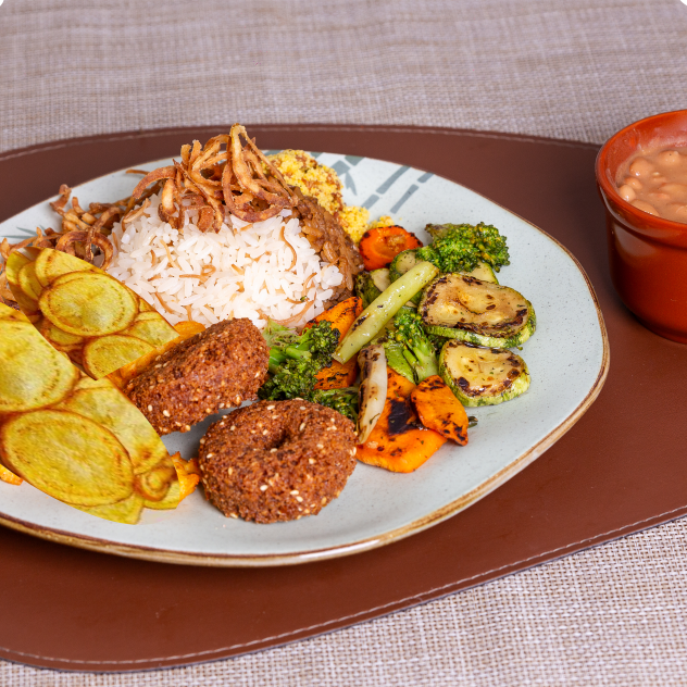 - Mjadara (arroz, lentilha e cebola crispy) - Arroz árabe (arroz com cabelinho de anjo) - Feijão com tempero árabe - Farofa fina de milho, soja, temperos e erva finas - 2 bolinhos de falafel - Mix de legumes salteados (abobrinha, cenoura, brócolis) e batata rústica com páprica e zaatar.