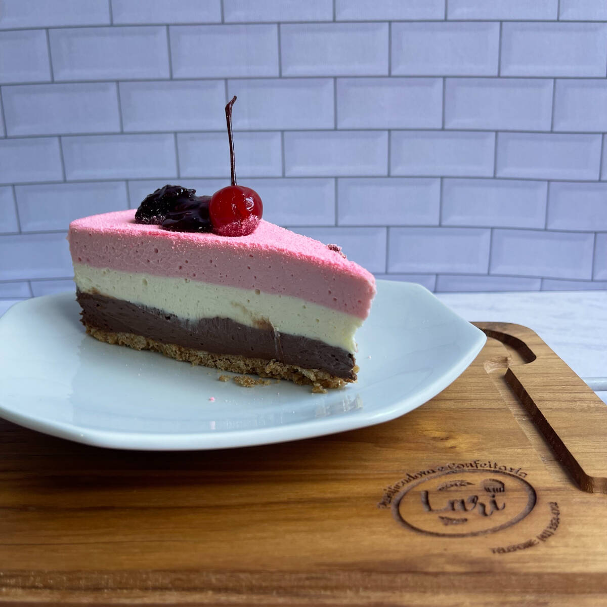 Uma fatia de tortaa com massa de bolacha, uma camada de creme de chocolate ao leite, uma de chocolate branco e outra de creme de morango.