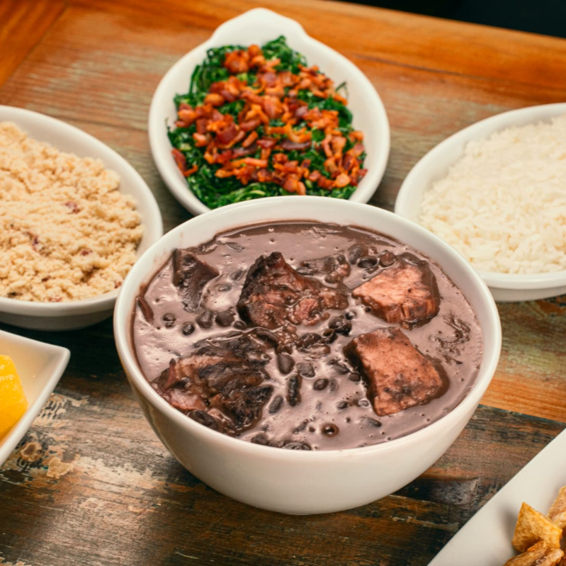 Feijoada com arroz branco, farofa com bacon, couve refogada, banana a milanesa, mini linguiças e laranja.