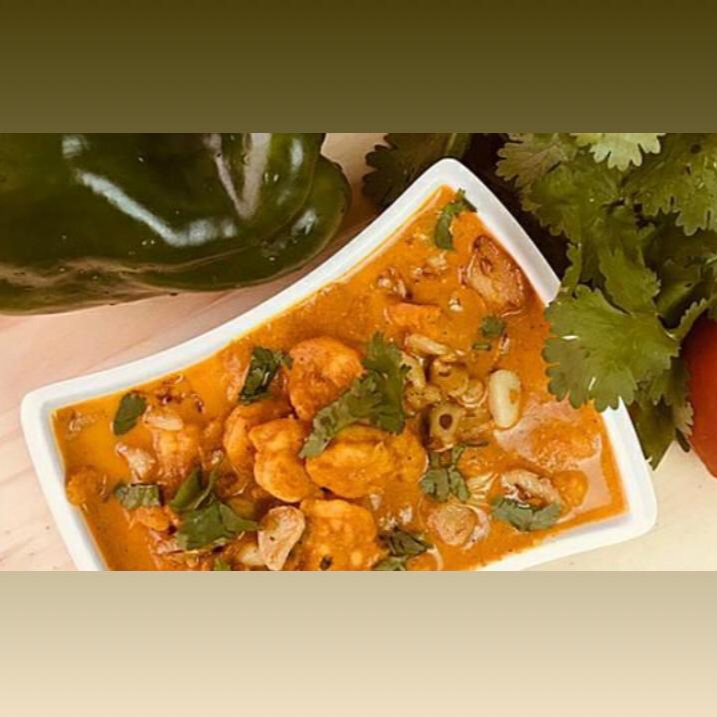 Camarões mergulhados em molho cremoso à base de leite de coco, curry e coentro. Indicação da compra de um pão para acompanhamento