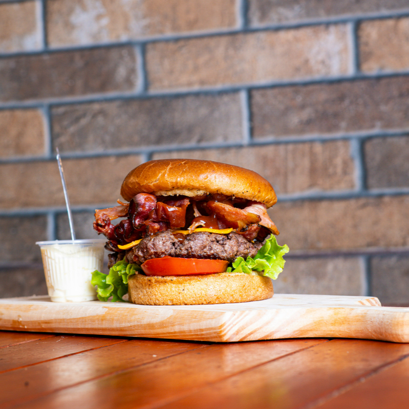Pão de Brioche, Blend bovino (120gr ou 160gr), Bacon Exagerado, Cheddar, Alface, Tomate, Maionese da Casa e Barbecue. . O 'Bacon do Rei' é uma soberba opção de hambúrguer artesanal. Apresenta um suculento blend de 120g, coberto com uma generosa camada de bacon crocante e exagerado, que simplesmente derrete na boca. É completado com uma fatia de cheddar derretido, adicionando uma cremosidade irresi
