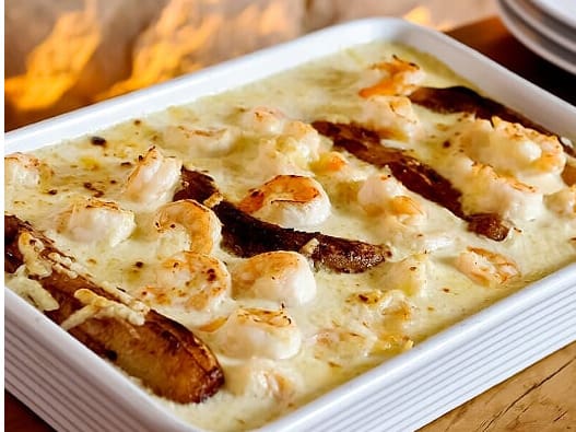 Tradicional receita cearense. Camarões servidos com molho a base de creme de leite ebananas fritas numa perfeita combinação. Gratinado com queijo parmesão. Acompanha arroz branco e batata gratinada.Tamanho do camarão nesse prato: 18g.