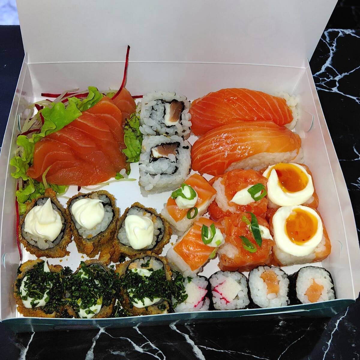 5 sashimis de salmão, 2 uramakis de salmão, 2 niguiris de salmão, 2 jhous de salmão, 2 jhous geleia de pimenta, 2 batera, 2 hossomaki de salmão, 2 hossomaki de kani, 3 hot roll com couve e 3 hot roll com cream cheese. Acompanha 2 hashis, 2 saches de molho shoyo e 2 saches de tarê.