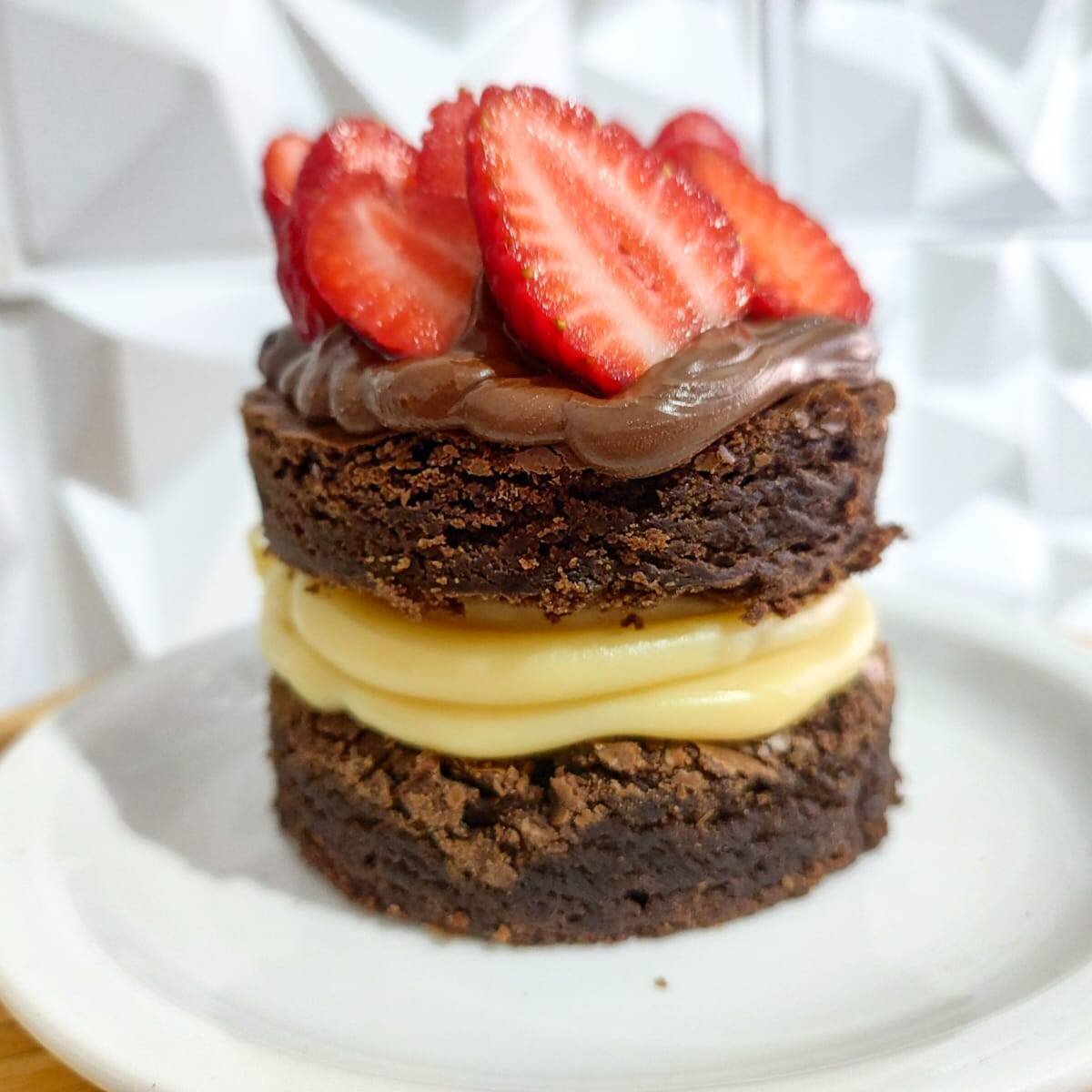 Brownie Gourmet de Ninho com Nutella e morango: dois discos generosos de brownie chocolatudo, recheio cremoso de Ninho no meio e uma cobertura irresistível de Nutella com morango fresco picado. Uma sobremesa grande, cremosa e feita para matar a vontade de doce de verdade, com 8,5 x 8,5 centimetros.