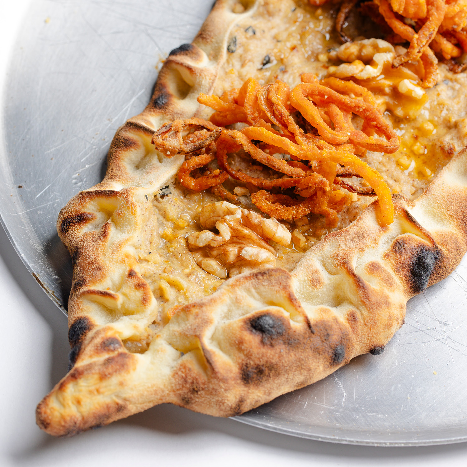 ESFIHA TURCA EM FORMATO DE BARCA, COM BERINJELA DEFUMADA, RASPAS DE LIMÃO SICILIANO, ESPECIARIAS E NOZES. VEGANA. CONTÉM GLÚTEN. CONTÉM OLEAGINOSAS.