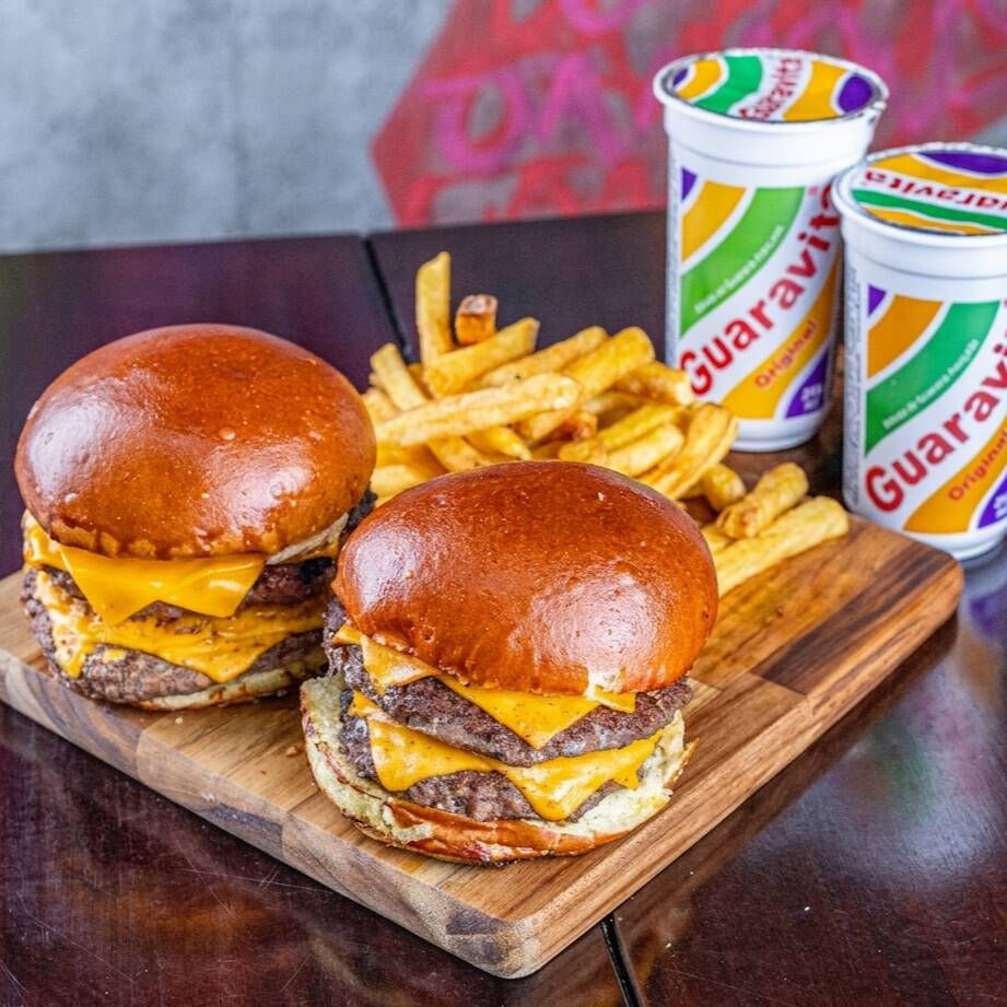 O Duplo Cheese é a escolha perfeita para os amantes de hambúrgueres repletos de queijo! Comece com um pão brioche artesanal, que abraça dois blends suculentos de 130g cada, grelhados ao ponto ideal para preservar sua suculência. Cada camada de carne é coberta por uma deliciosa fatia de cheddar derretido, que envolve seu paladar com um sabor cremoso e irresistível. A cada mordida, você sentirá a combinação perfeita entre o sabor da carne e a riqueza do queijo. Se você não resiste ao poder do queijo, o Duplo Cheese é a opção certa! São 2 Cheeses acompanhado de batata chips crocante e 2 Guaravitas