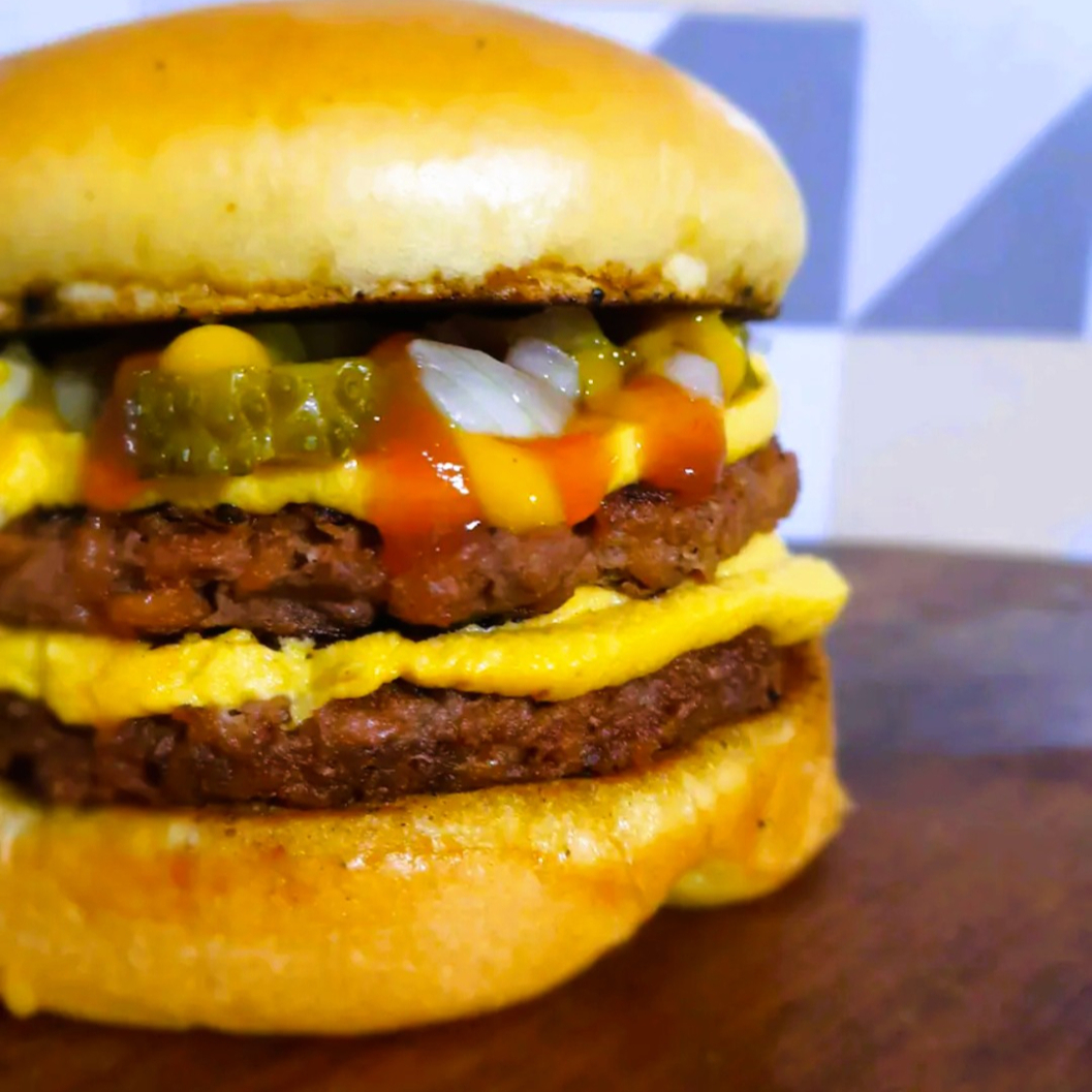 2 x burgers sabor carne feito com proteína de ervilha (não contém soja) + queijo tipo cheddar de castanha de caju + cebola + ketchup + mostarda + picles de pepino no pão de brioche selado na chapa!