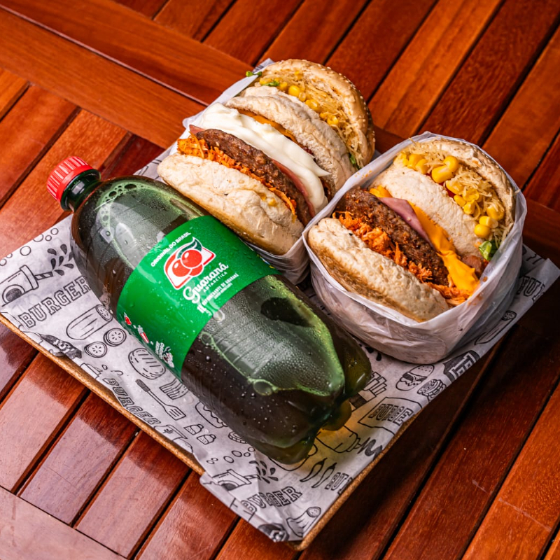 X TUDÃO ( Pão artesanal, carne de hambúrguer bovino, queijo prato derretido, ovo frito, bacon em cubos, presunto, frango desfiado, catupiry ou cheddar, batata palha fina artesanal, milho verde, alface crespa e tomate fresco) acompanha 1 guaraná 1l. Escolha entre cheddar e catupiry na observação