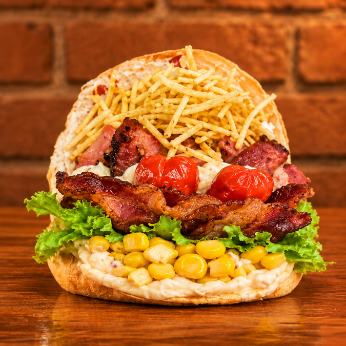 Pão com filé de frango, bacon, queijo, presunto, abacaxi, salada, milho e batata. Uma combinação caprichada que une o sabor do bacon ao toque do abacaxi em cada mordida!