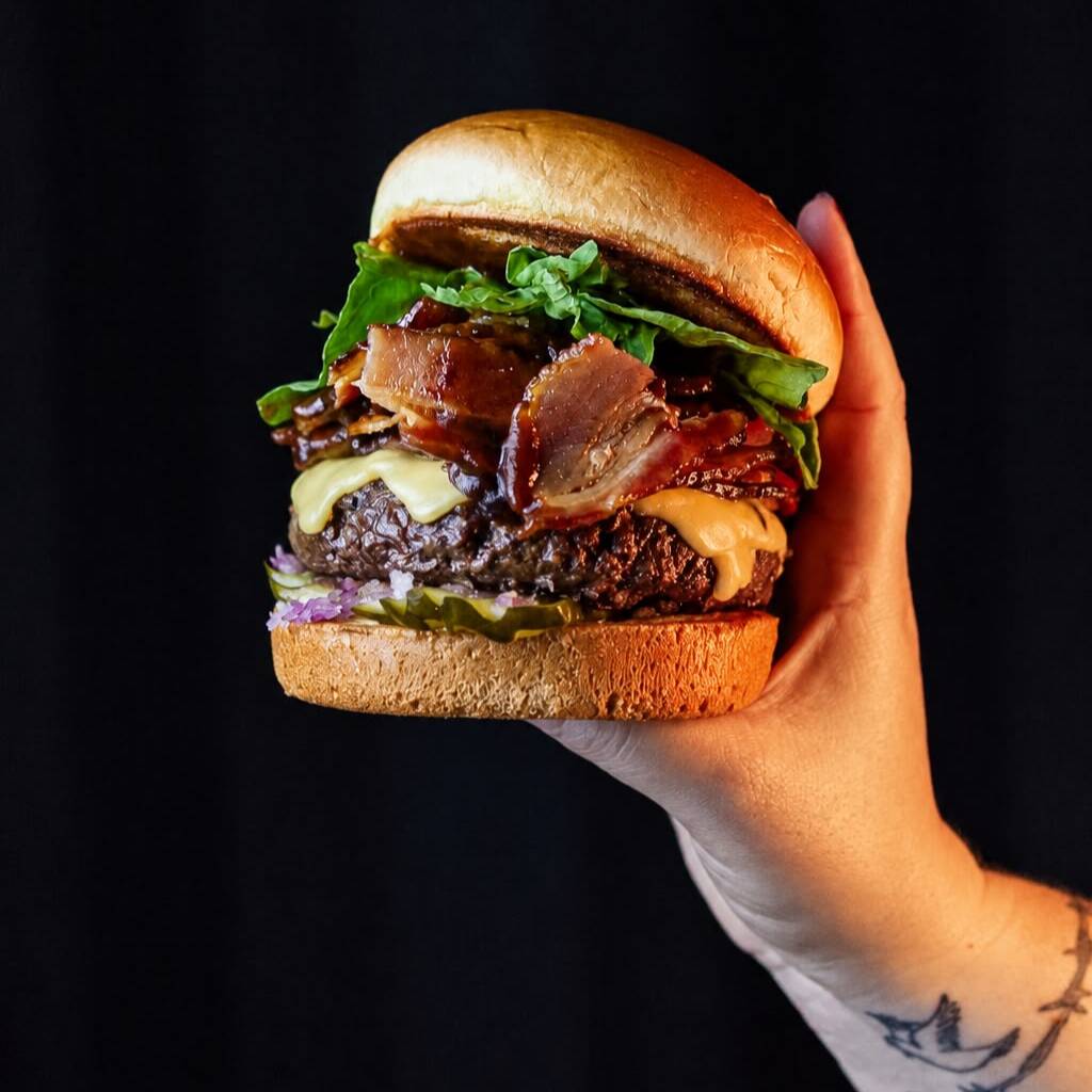 Pão de brioche, picles, cebola roxa crua, hambúrguer 180g(in natura), queijo prato, muito bacon, barbecue e rúcula.