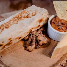 Delicie-se com nosso 'Burrito de Carne Grelhado - Machete honegem ao filme de Danny Trejo', Este Burrito apresenta uma tortilha de trigo macia e fresca, habilmente enrolada e generosamente recheada com queijo derretido, proporcionando cremosidade em cada mordida. O Pico de Gallo, vinagrete fresco e vibrante, adiciona um toque picante, enquanto o Chili, uma combinação de carne com feijão levemente apimentada, traz a tradição mexicana. A carne, marinada com um blend de especiarias secretas e cortada em filetes no estilo da casa.