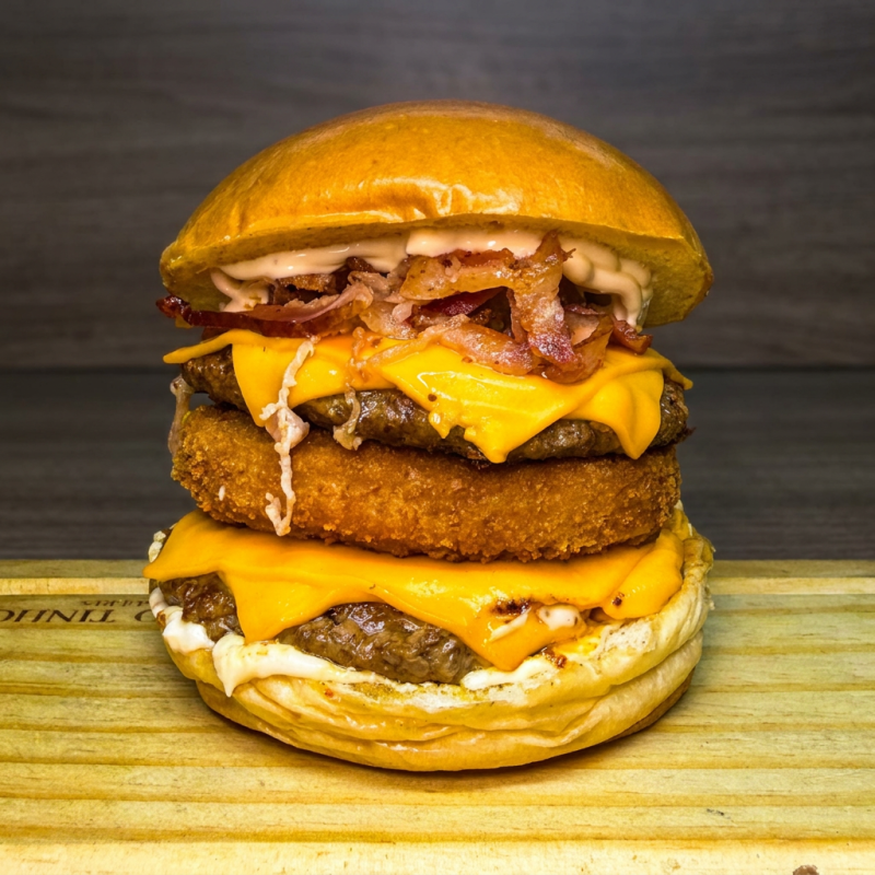 Pão super de Brioche super macio , disponível também na opção de gergelim, 2 suculentos burguer de 120g, 1 burguer de frango crocante, bacon fatiado , fatias de queijo cheddar e molho da casa