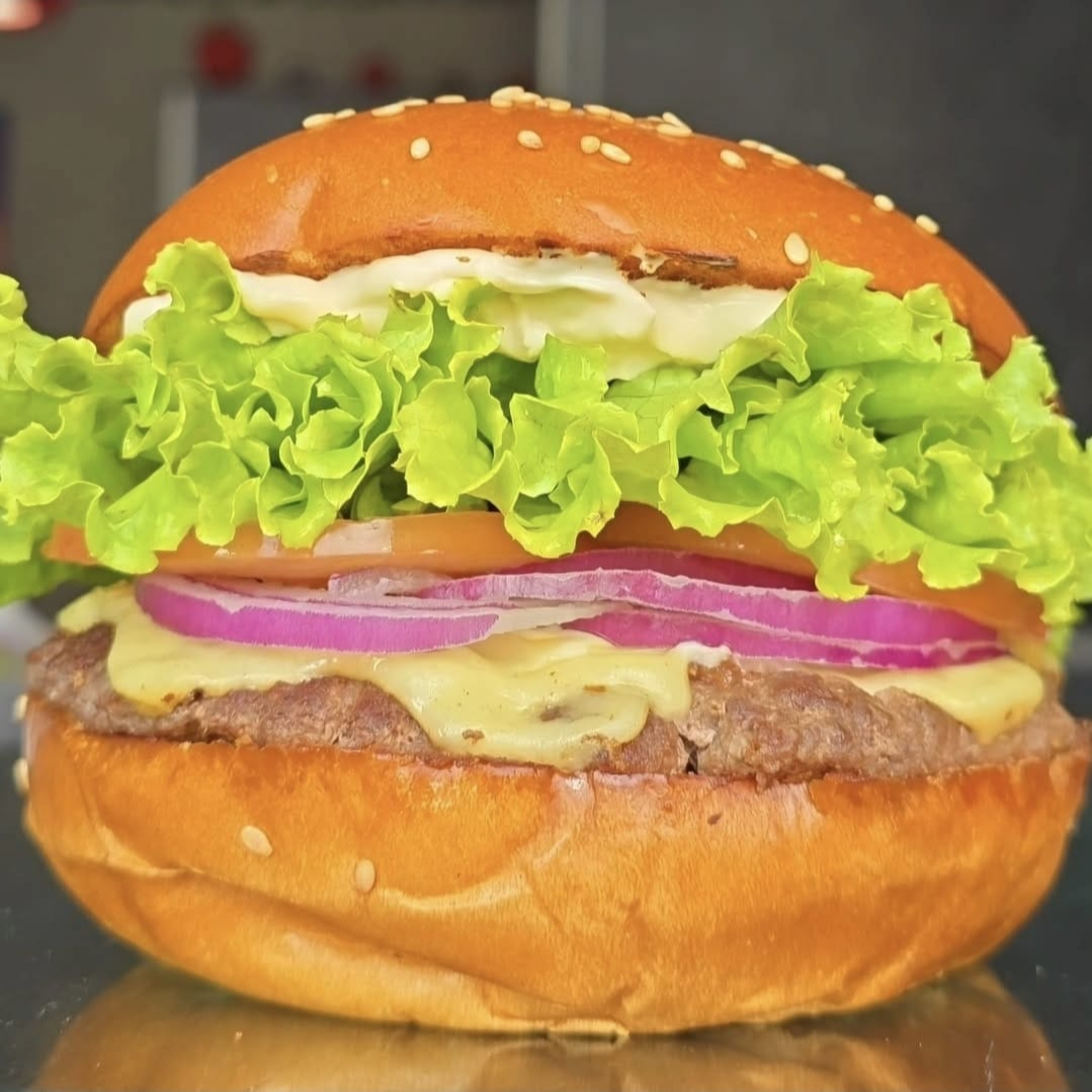 Burger Fininho de 100g (Fake Smash) feito no charbroiler, 2 fatias de queijo prato top, aquela salada bem fresquinha (alface, tomate e cebola roxa crua), molho the best suculento em um pão brioche artesanal com gergelim bem fofinho. Obs.: não alteramos o queijo e nem o ponto da carne.