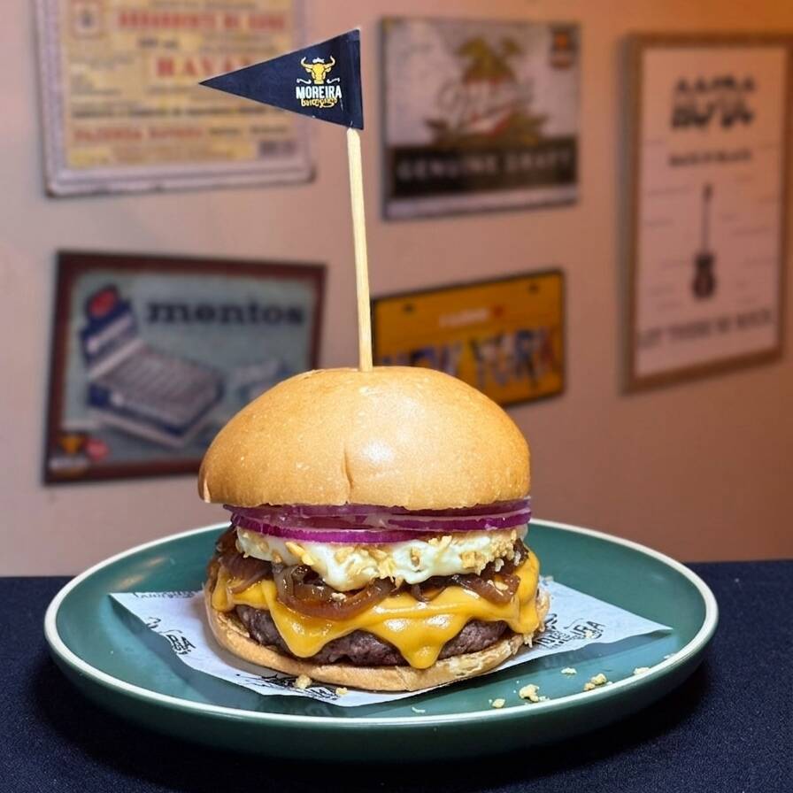 Suculento Burger Angus, Fatias de Queijo, Cheddar Americano, Requeijão Cremoso, Cebola Caramelizada, Alho Frito, Cebola Crua, Mostarda e Maionese. Servido no Pão Levemente Selado