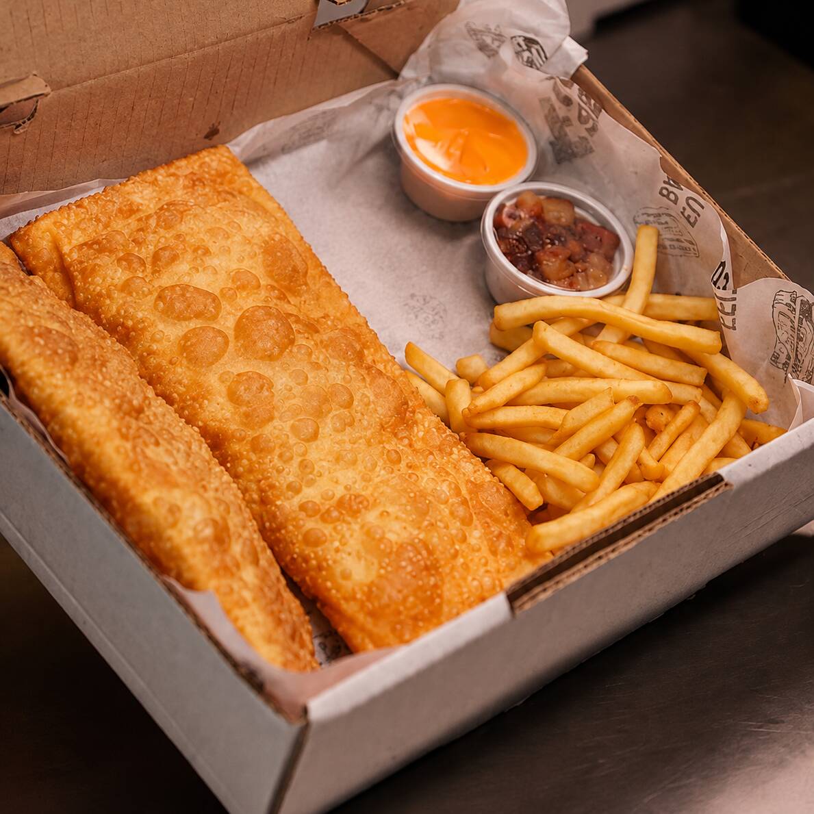 Dois pastéis grande uma porção de batata e molho ketchup e maionese.