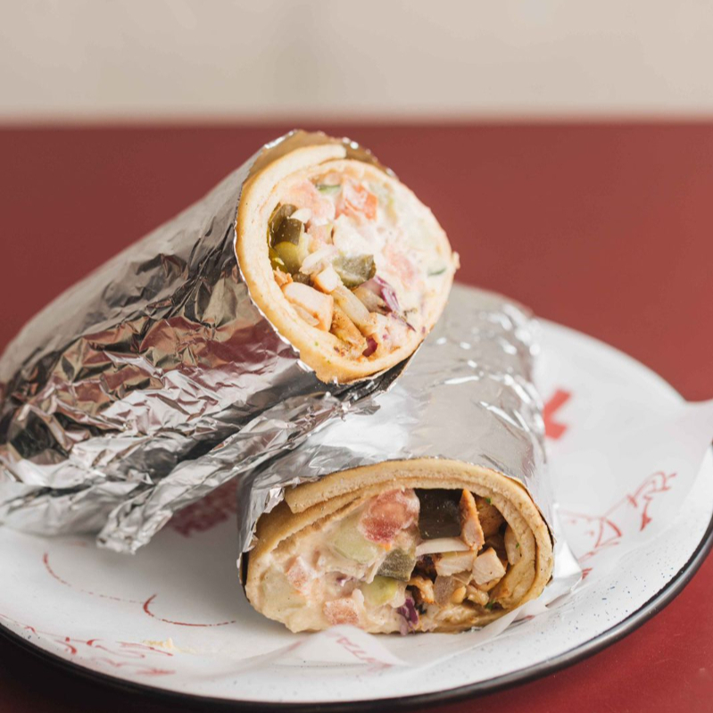 Coxa e sobrecoxa de frango temperada, cebola na chapa, salat israeli (tomates e pepinos em cubos), hummus, tehina, repolho e picles de pepino, servido na lafa.