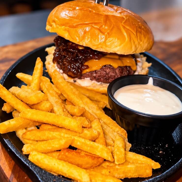 Pão brioche selado, hambúrguer artesanal de 160g, com maionese artesanal, com queijo cheddar em fatias, fatias generosas de bacon grelhados na brasa e cebola caramelizada. Acompanha 100g de batata fritas.