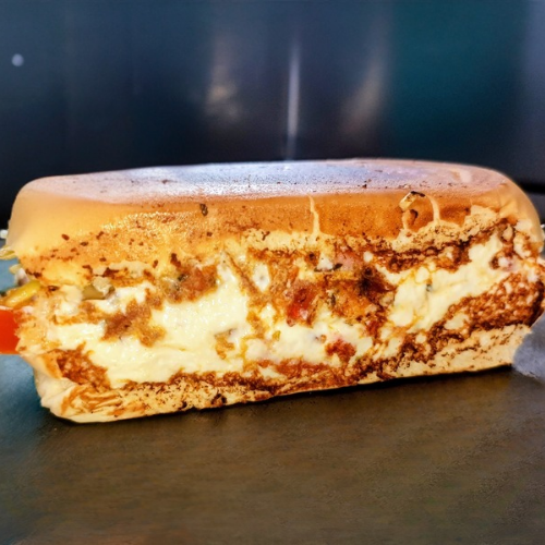 Uma experiência única com sabor de pizza, incluindo pão, duas salsichas Perdigão, presunto, mussarela, tomate, cebola, milho, orégano, ketchup, mostarda, cream cheese (Philadelphia) e batata palha.