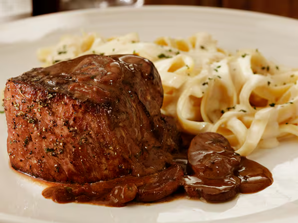 Filet mignon grelhado com cerca de 230 g, servido com molho de vinho marsala, prosciutto e cogumelos salteados. Acompanhamento à sua escolha.